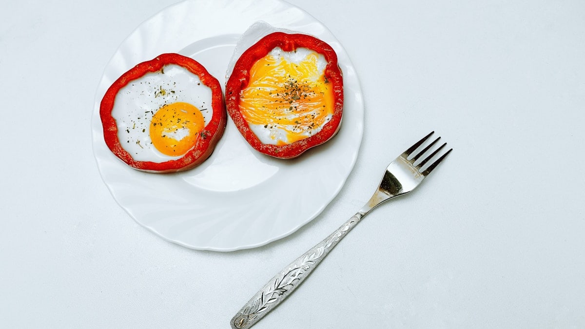 Bright and juicy picture with orange eggs and red sweet pepper. The eggs are on a plate, next to the plate there is a fork. Beautiful frame with appetizing food.